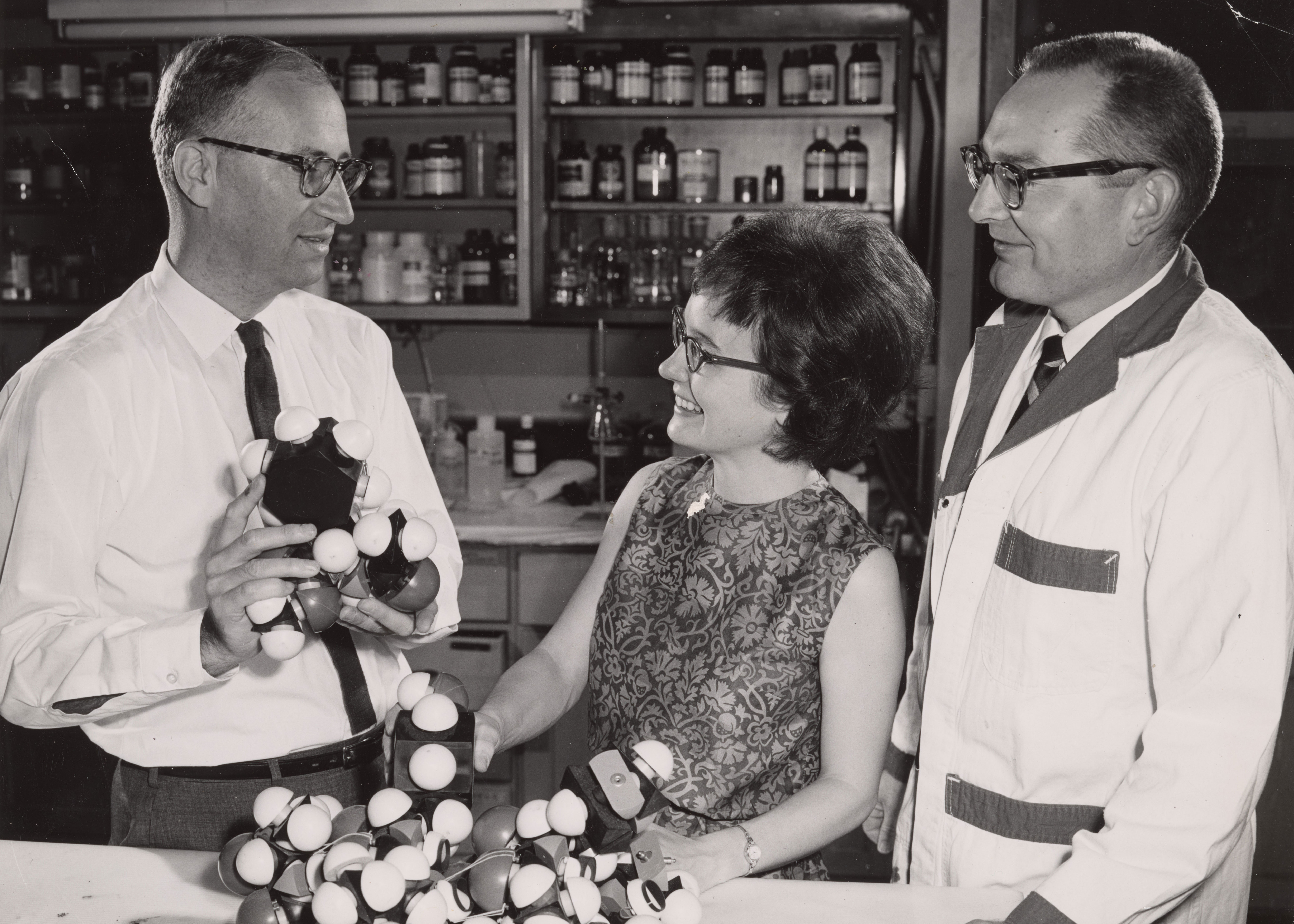 Daniel Koshland stands in front of a man and a woman and gestures toward a DNA model