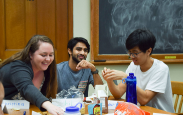 A student reaches across a table with two other students to her right