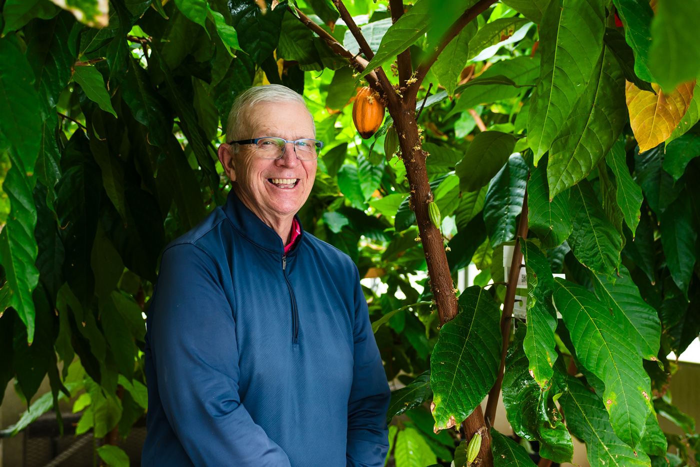 A photo of a man among potted trees smiling.