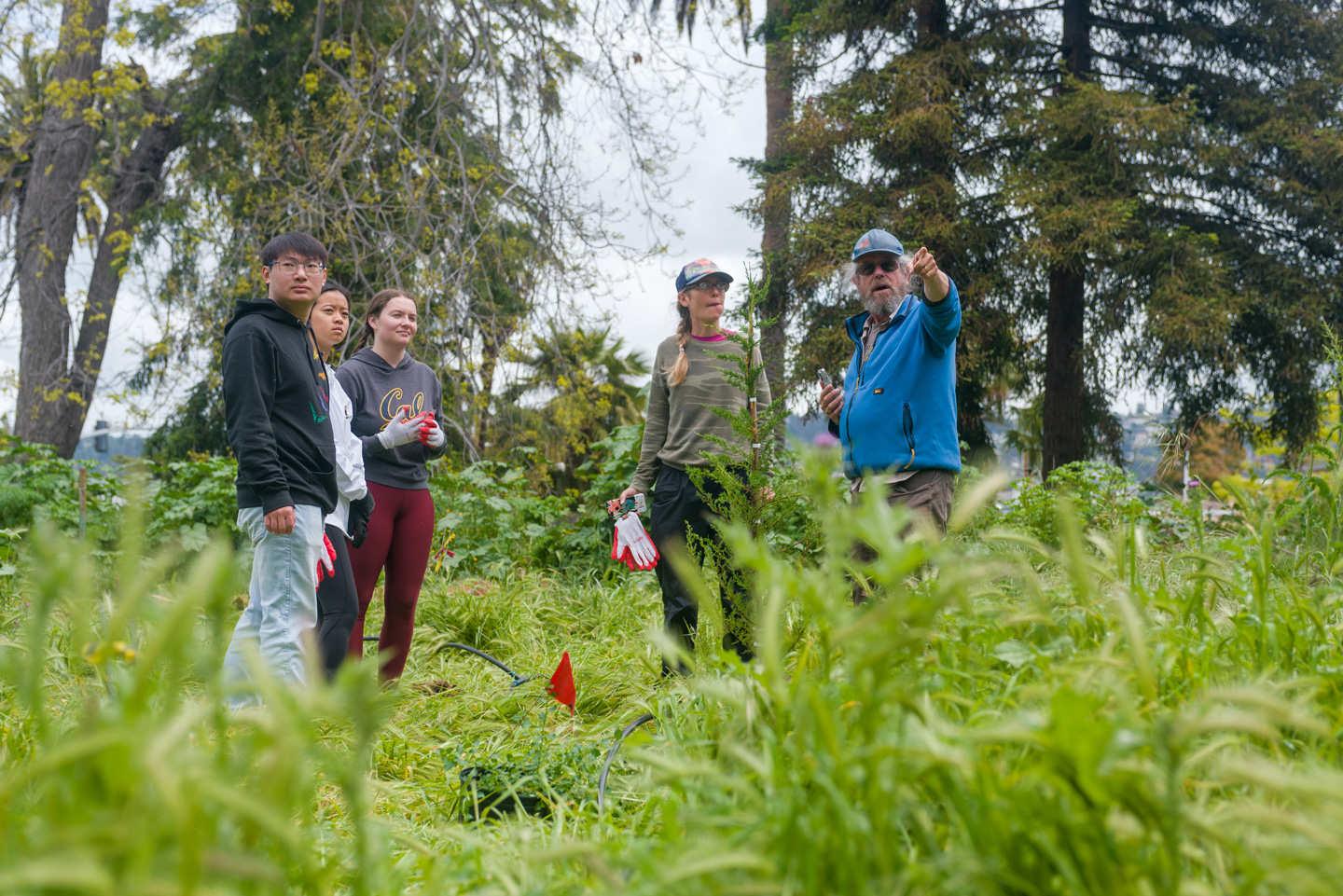 A man in a blue hat and sunglasses points toward the direction of the camera directing a group of volunteers.