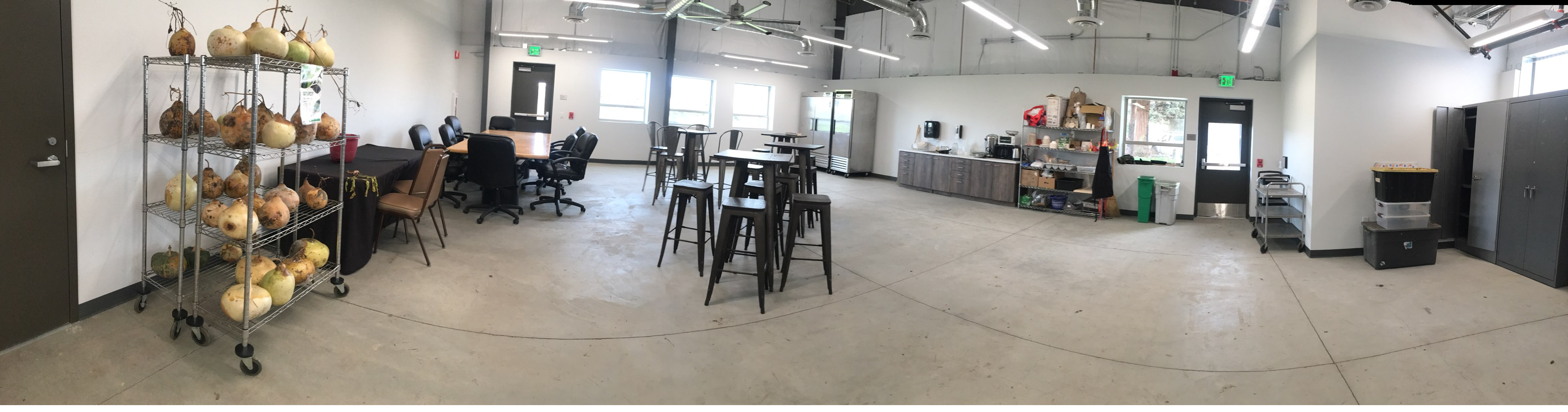 Wide angle shot of conference room with tables, chairs, and a small kitchen