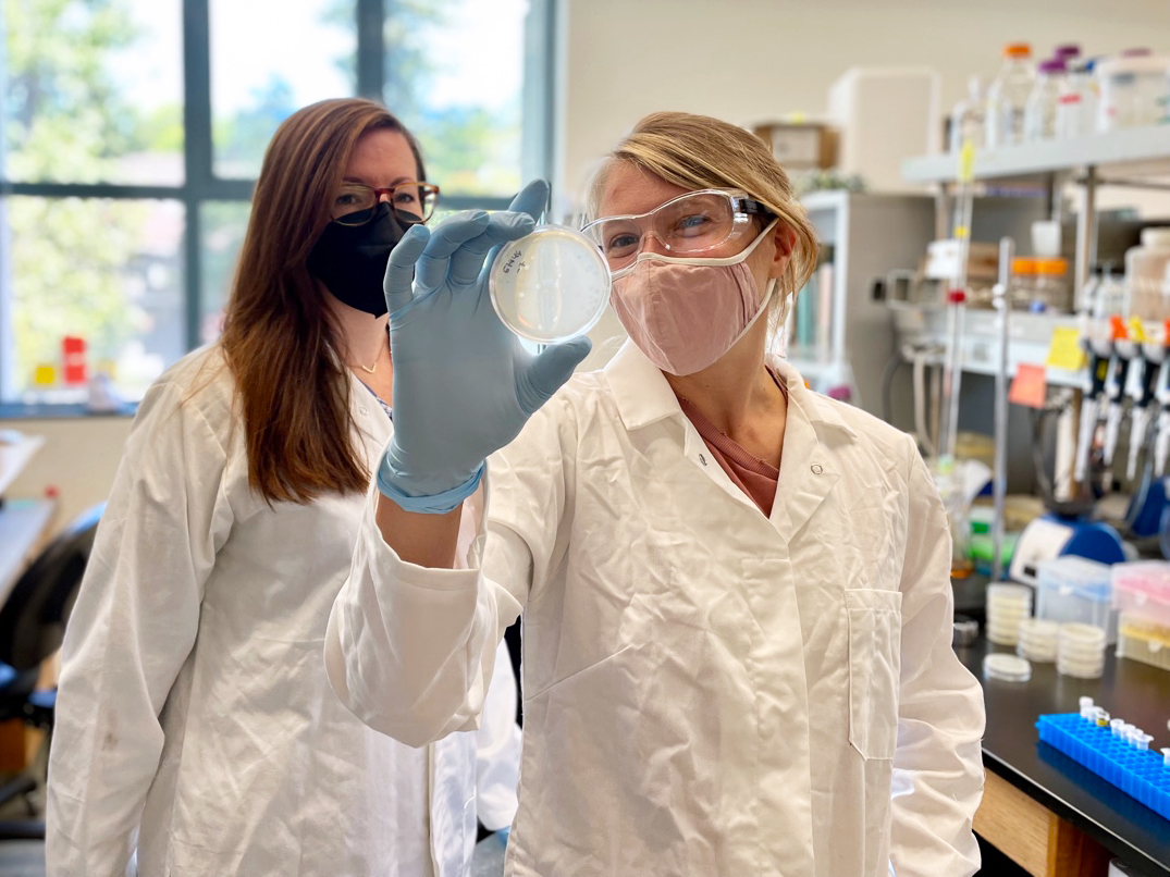 Two researchers wearing masks holding up a petri dish