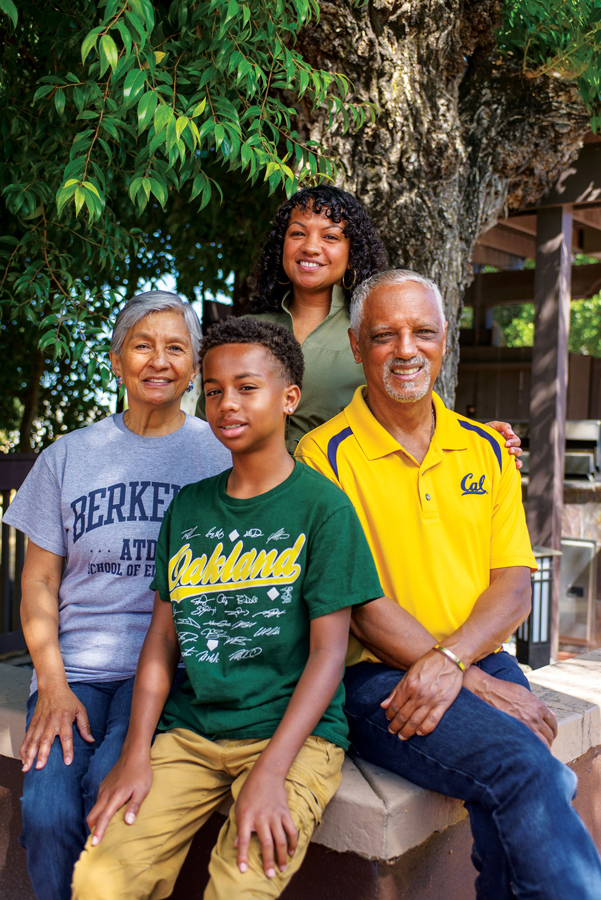 A photo of four people sitting on a brick wall under the shade of a tree.