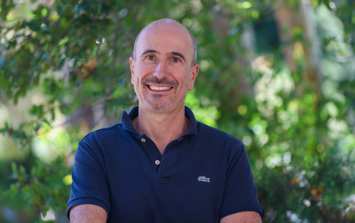 A headshot of a smiling Paolo D'Odorico, standing outdoors in front of green foliage.