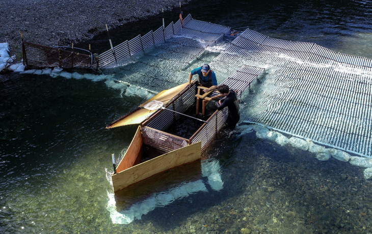 A photo of two men examining a metal structure in a river.