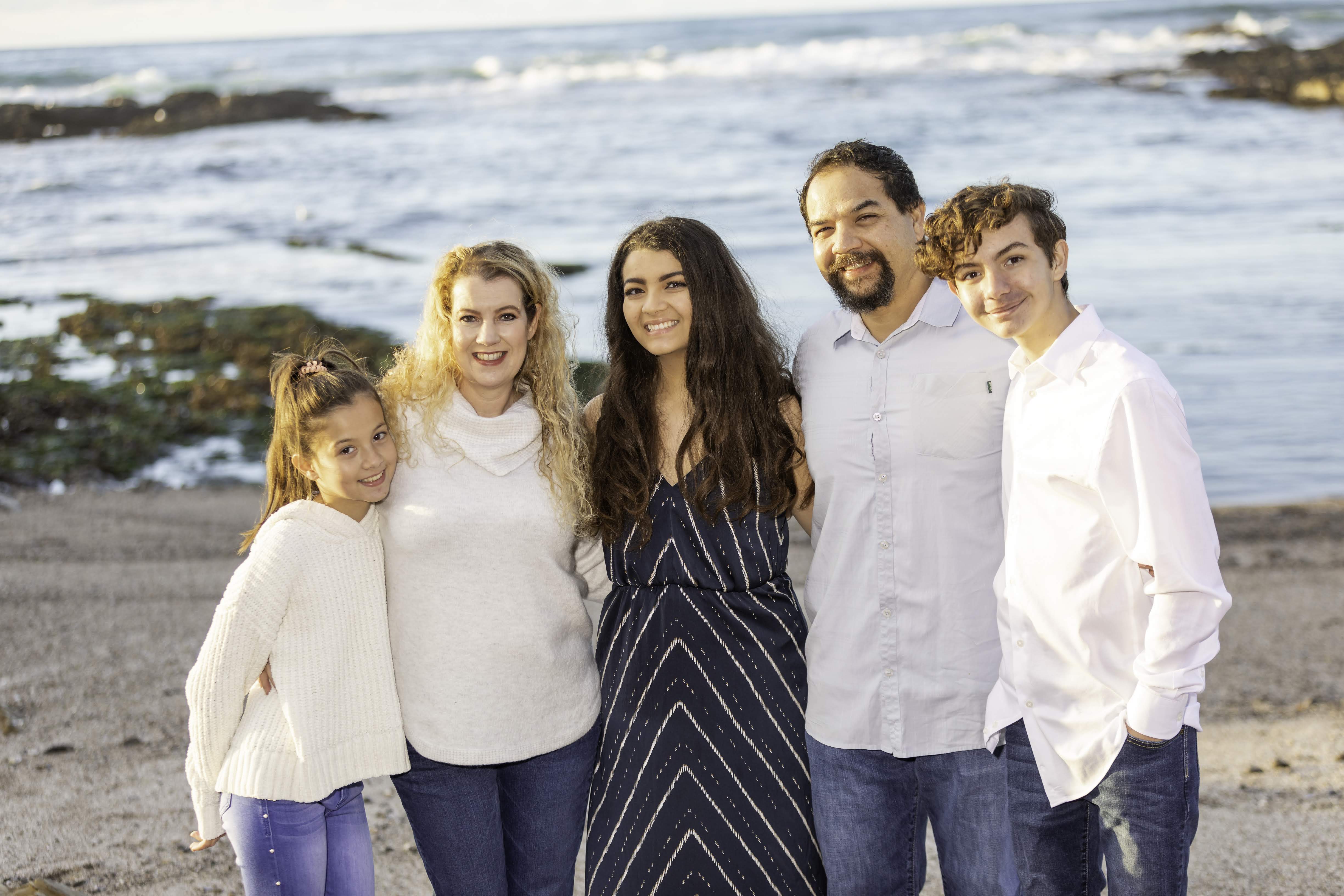 A photo of a group of people smiling at the camera. The ocean is visible behind them.