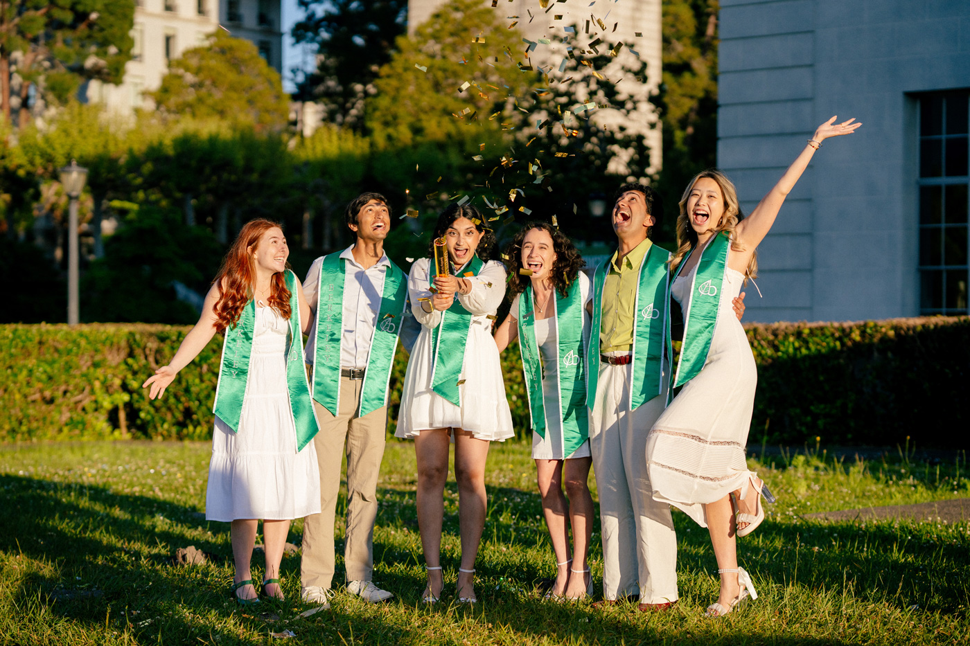 A group of men and women wearing graduation clothes celebrate using confetti