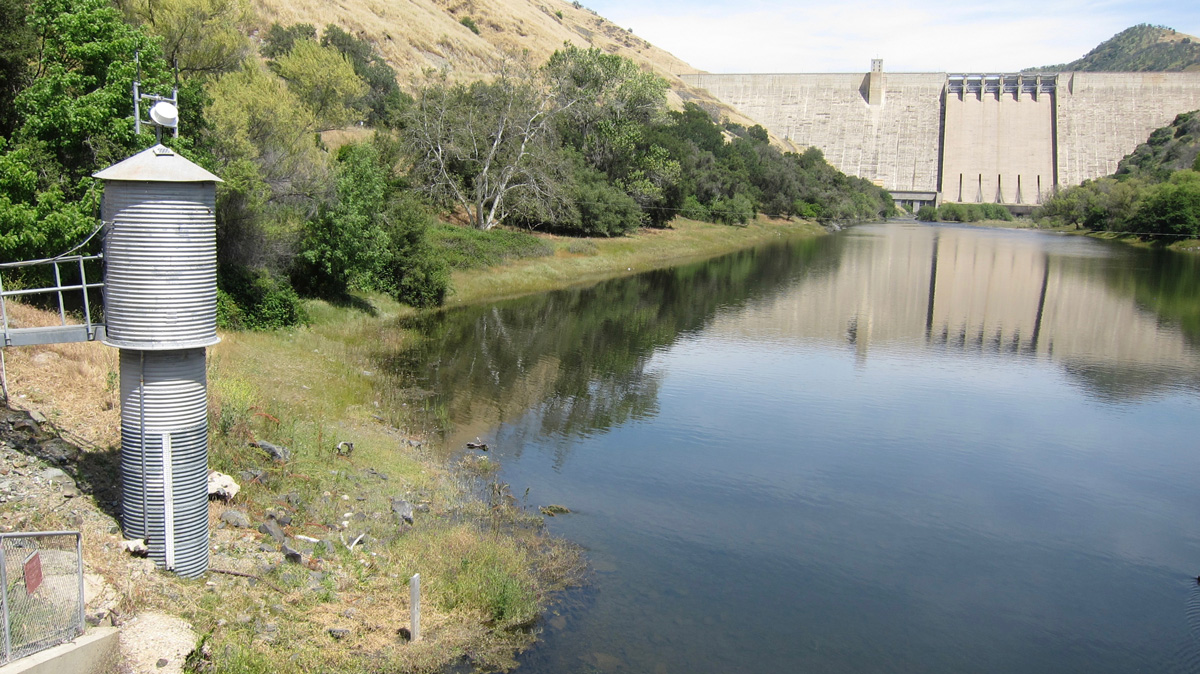 A photo of a metal structure on a riverbank in front of a concrete dam