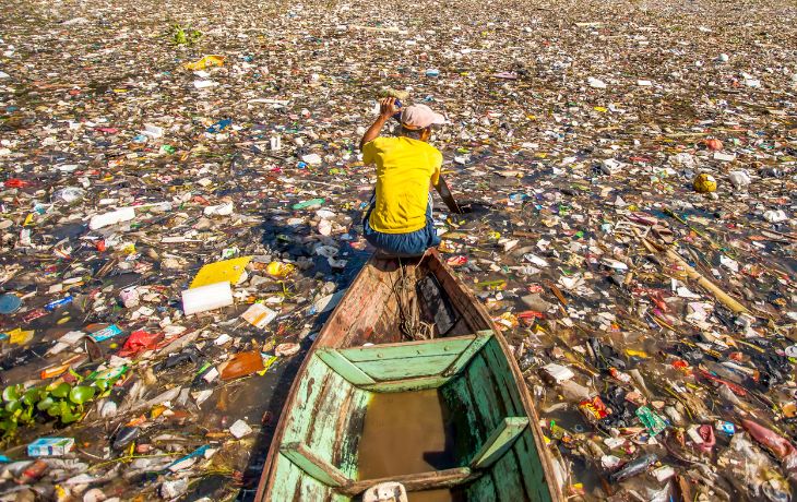 Adobe stock image of man on boat, surrounded by a pool of plastic and waste.