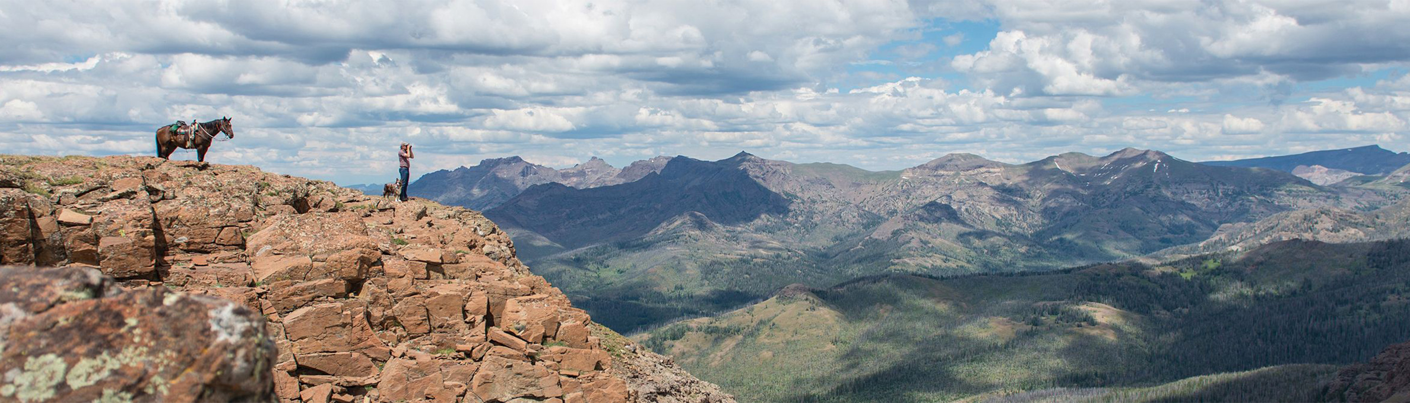 A man standing on top of a mountain looking out into the valley with binoculars
