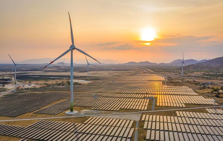 An aerial photo of solar panels and windmills taken during the early evening.