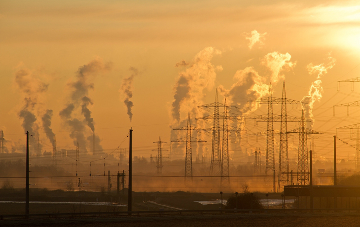A photo of electric transmission lines at golden hour with smoke visible in the sky.