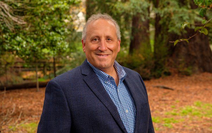 A photo of Professor Allen Goldstein smiling at the camera against a wooded backdrop.