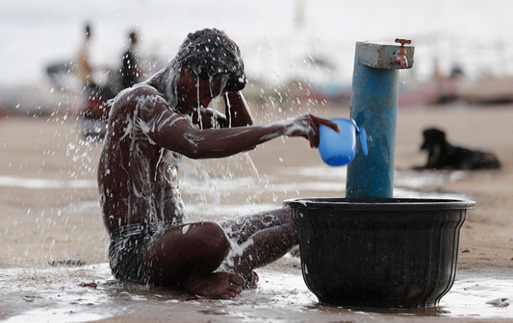 An Indian man pouring water on himself at a public fountain.