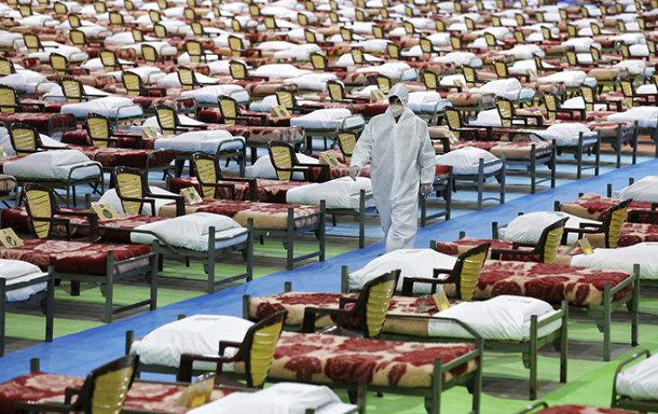 Empty hospital beds in Iran and a worker in full protective equipment