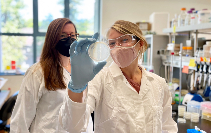 Two researchers wearing masks holding up a petri dish