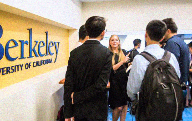 A woman speaking to two students next to a Berkeley sign.