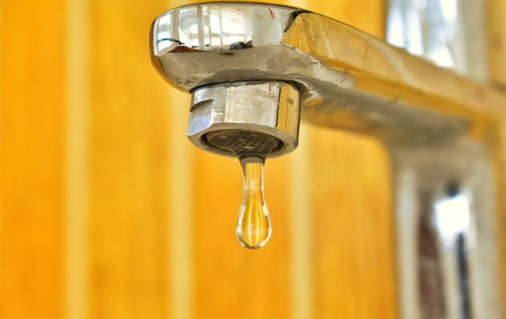 Slightly rusted water faucet dripping a drop of water