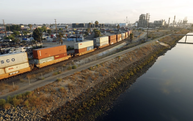 A railroad with cargo on it shown beside a large waterway.