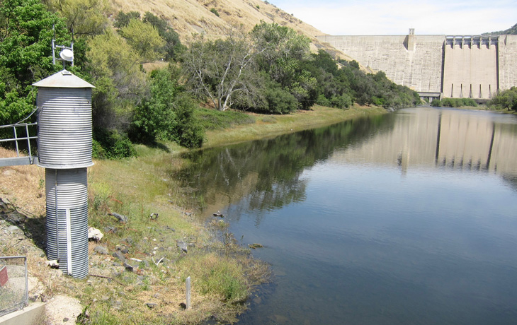 A photo of a metal structure on a riverbank in front of a concrete dam