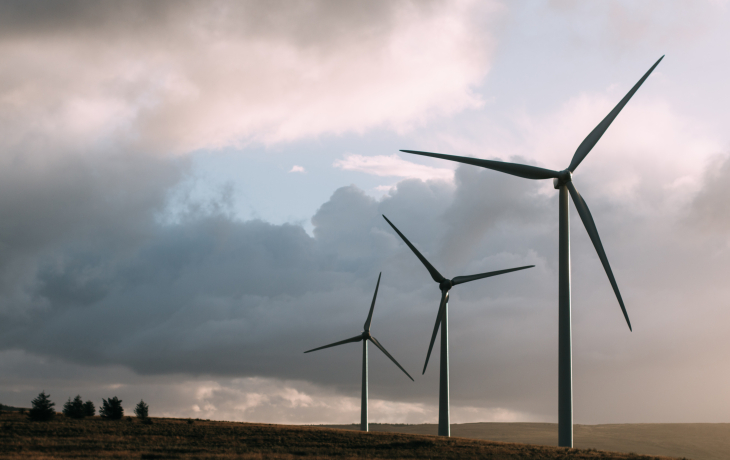 Three wind turbines standing in a flat field, under cloudy skies. 