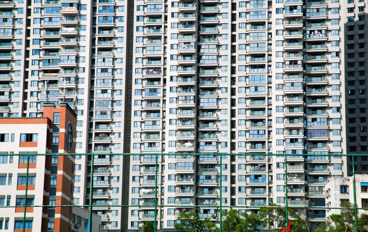 An apartment building showing rows of windows and trees in the foreground 