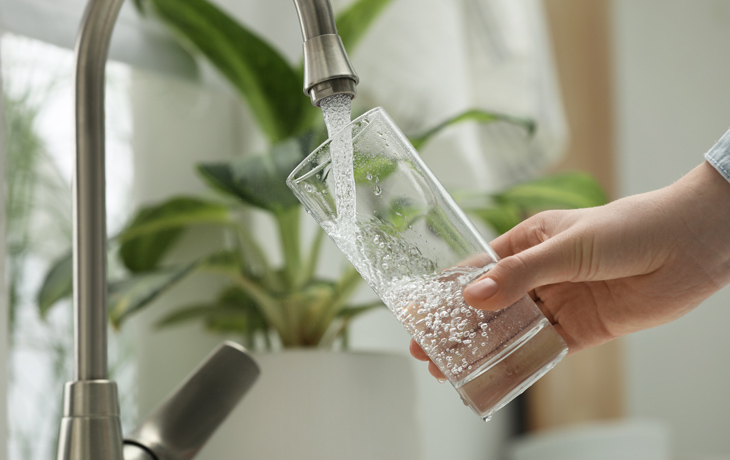 A close-up photo of a person filling glass with water from tap at home.