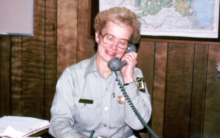 Geri Bergen sitting at a desk with papers around her. She is on the phone. 