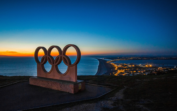 Olympic "rings" symbol sign in front of city landscape at night