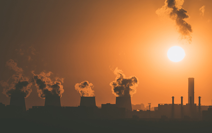 Orange skyline showing smokestacks emitting carbon in distance