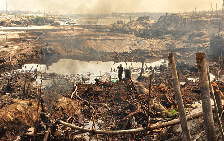 Landscape of a large pit mine with a worker drinking coffee in foreground