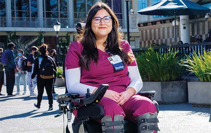 Alena Morales in medical scrubs while sitting in a wheelchair in front of Golden Bear Cafe.