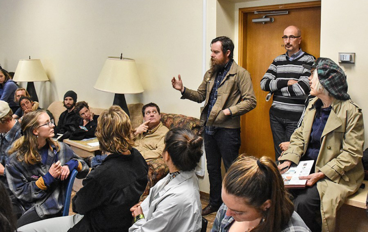 A person stands before a room full of people and gestures while speaking