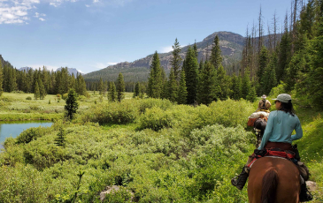 Two people riding horses shown from behind with a beautiful landscape